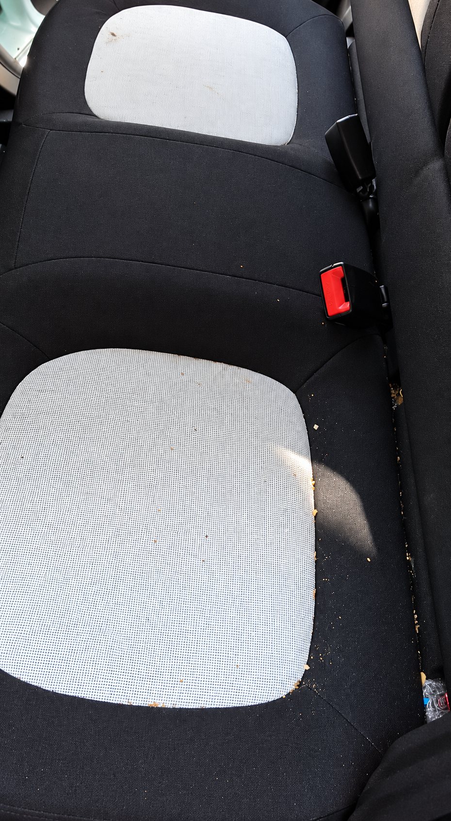 Vue de dessus d'une banquette arrière de voiture en tissu noir et gris clair, parsemée de miettes et de saletés, avant un nettoyage.