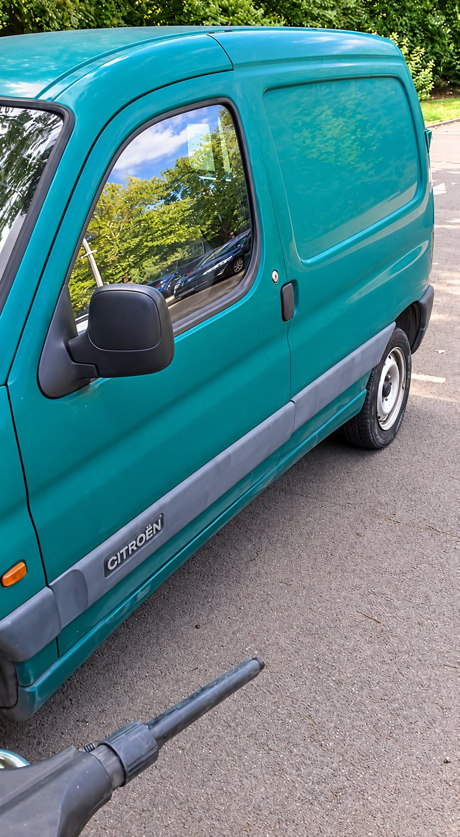 Une camionnette utilitaire Citroën verte, garée sur un parking, avec au premier plan la lance d'un nettoyeur haute pression.