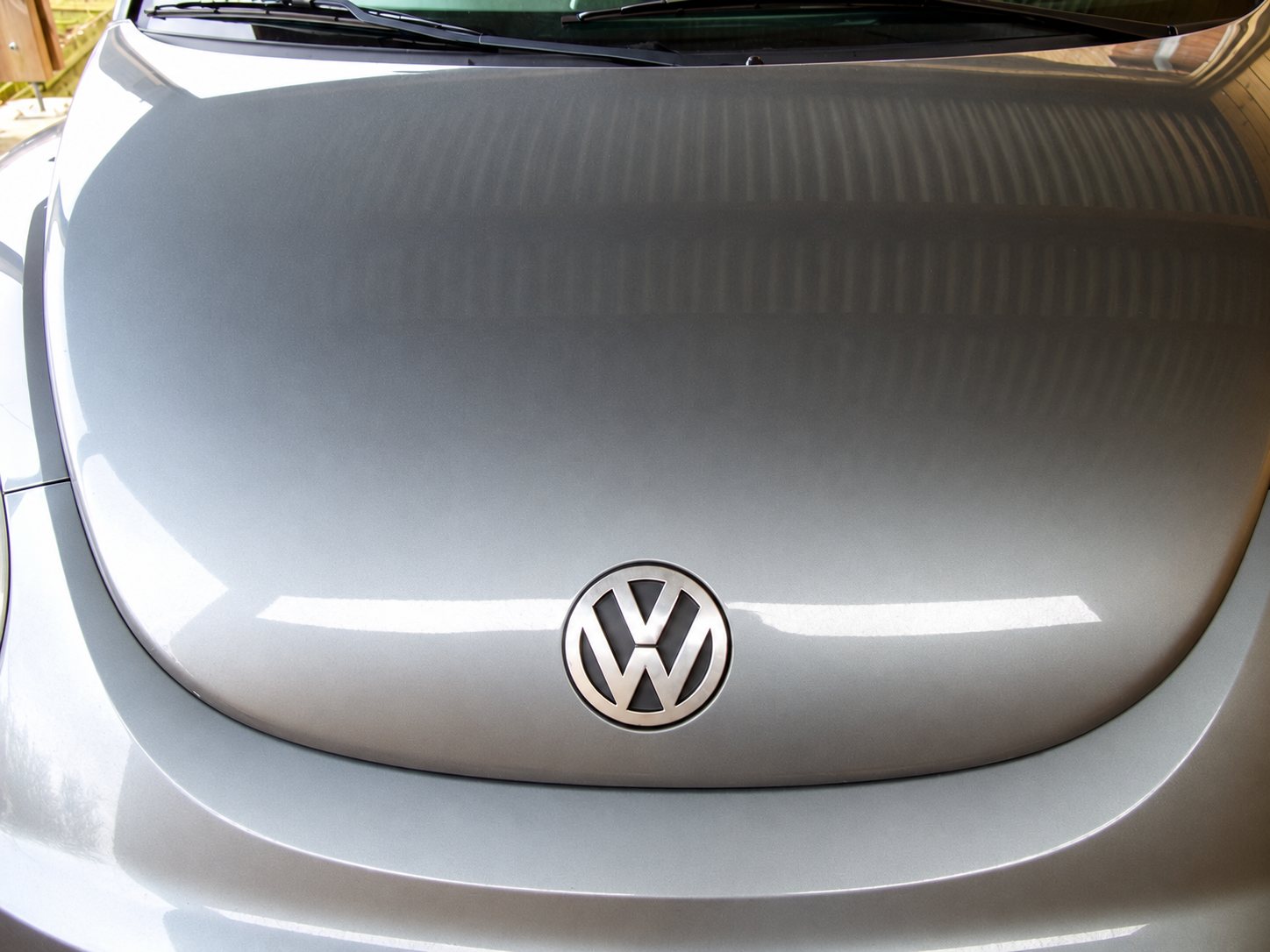 Gros plan sur le capot gris et poussiéreux d'une Volkswagen avec le logo VW chromé au centre.