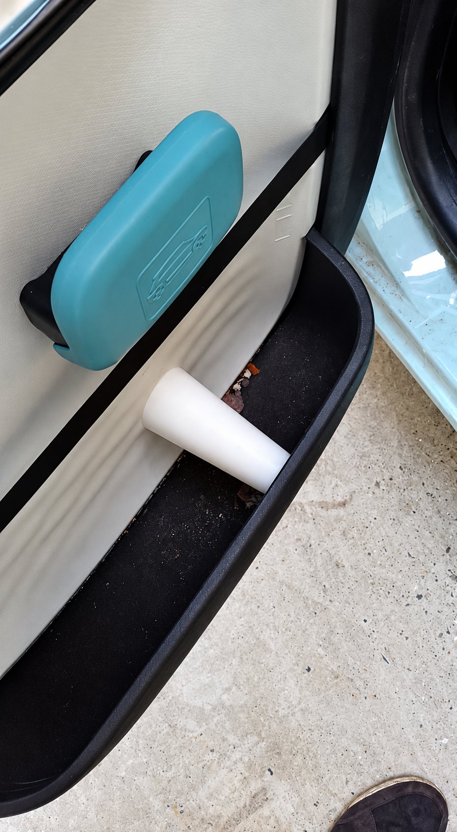 Gros plan sur l'intérieur d'une portière de voiture ouverte, avec une poignée turquoise et un embout blanc posé dans le rangement noir.