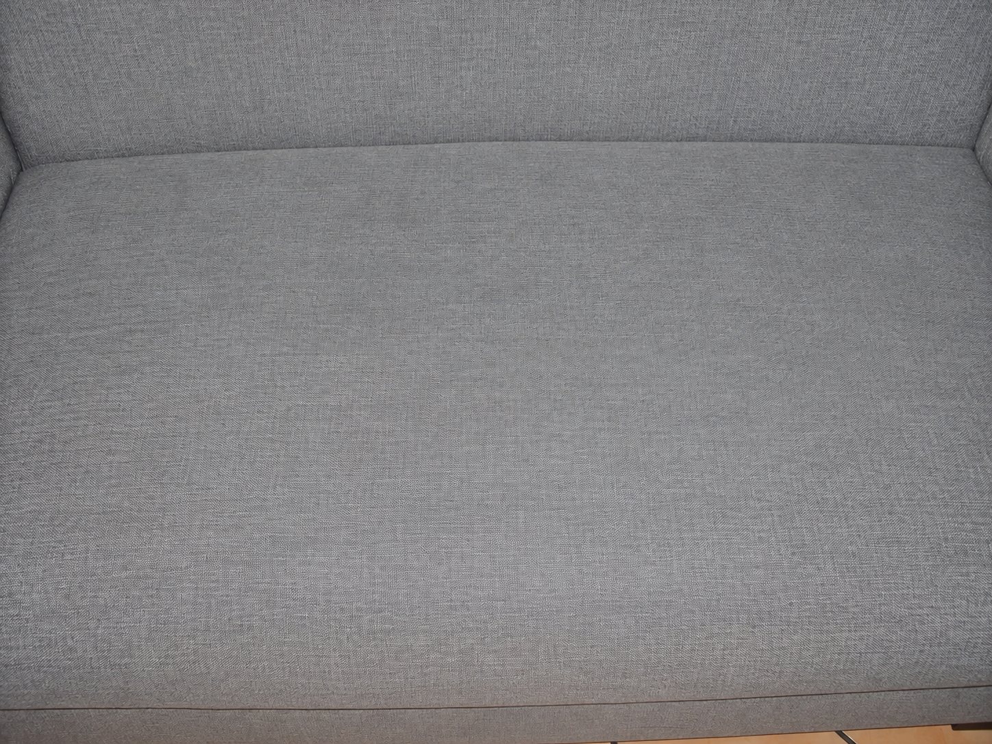 Gros plan sur le tissu gris-bleu d'une assise de canapé, avec des zones légèrement plus claires qui évoquent un nettoyage.