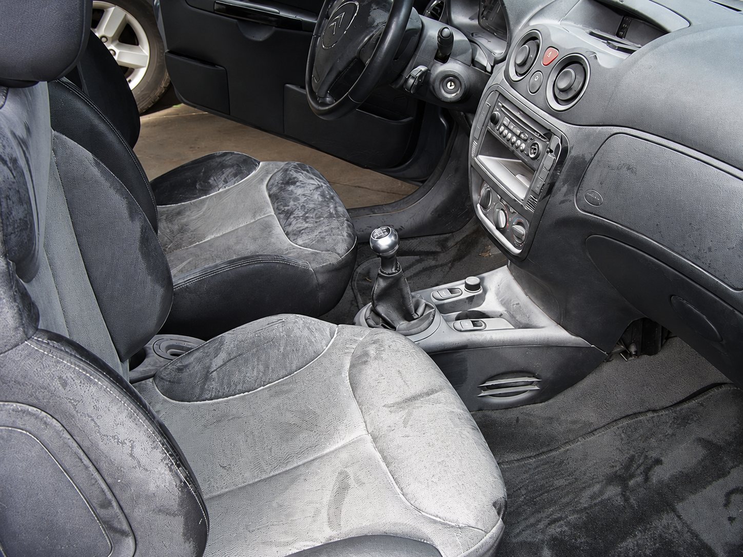 Intérieur d'une voiture avec sièges, levier de vitesse et tableau de bord recouverts d'une poudre grise et de saletés.