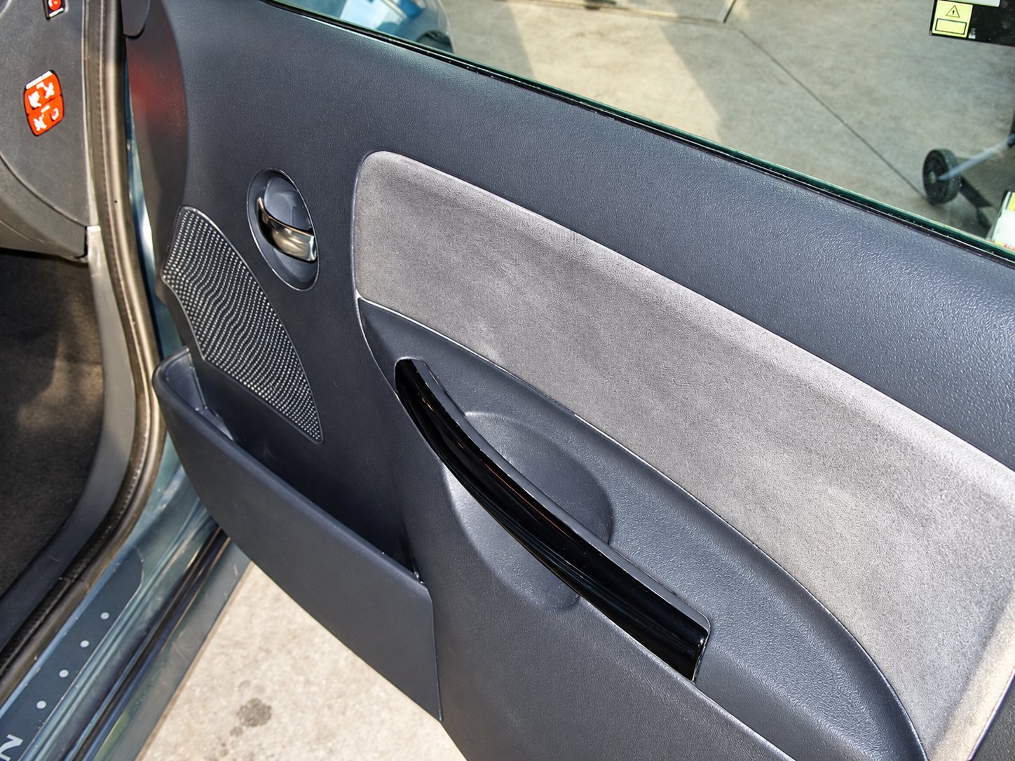 Gros plan sur le panneau de porte avant droite d'une voiture grise, avec poignée noire brillante, haut-parleur et garniture en tissu.