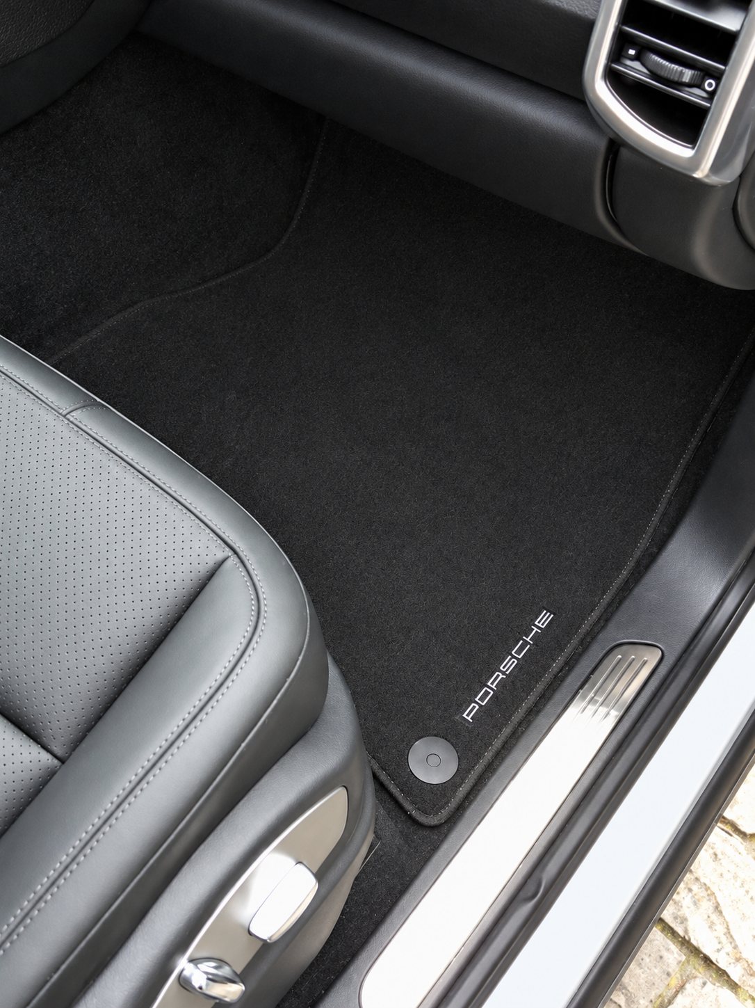 Tapis de sol en moquette noire siglé Porsche, posé devant un siège en cuir noir et un seuil de porte métallique.