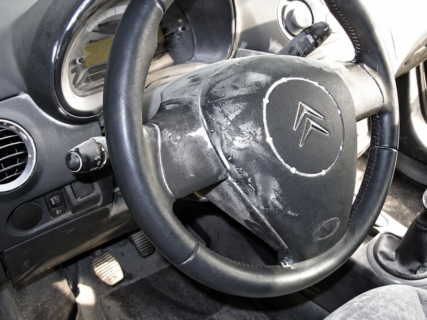 Gros plan sur le volant et le tableau de bord d'une Citroën dont les surfaces sont couvertes de mousse de nettoyage blanche.