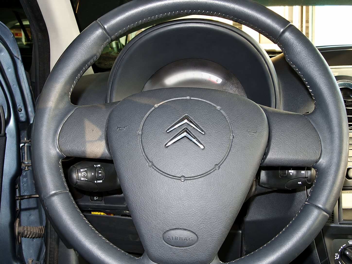 Gros plan sur le volant en cuir gris d'une Citroën, avec le logo à chevrons sur l'airbag et les commandes au volant.